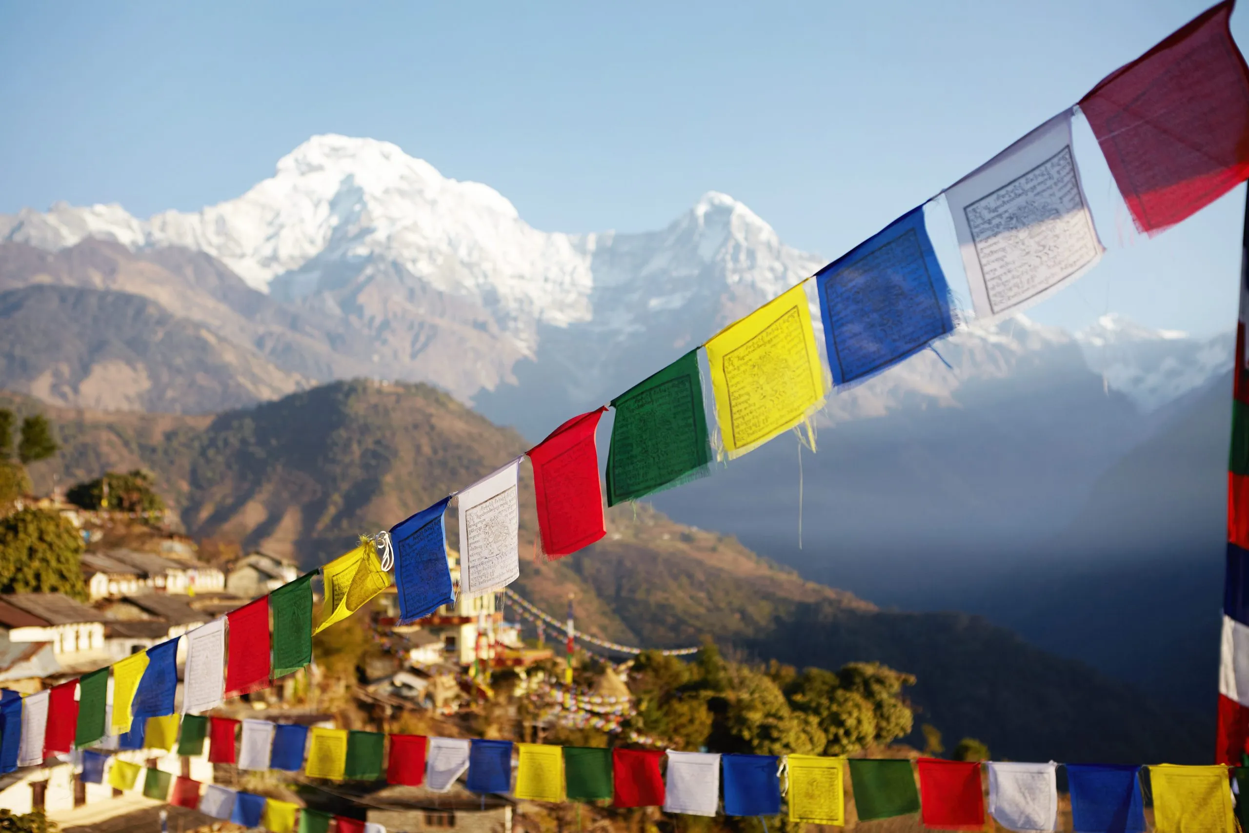 Spectacular view of grand snow capped summits of the Himalayan mountain range rising above in background, with rows of colorful Buddhist prayer flags strung along mountain passes in foreground